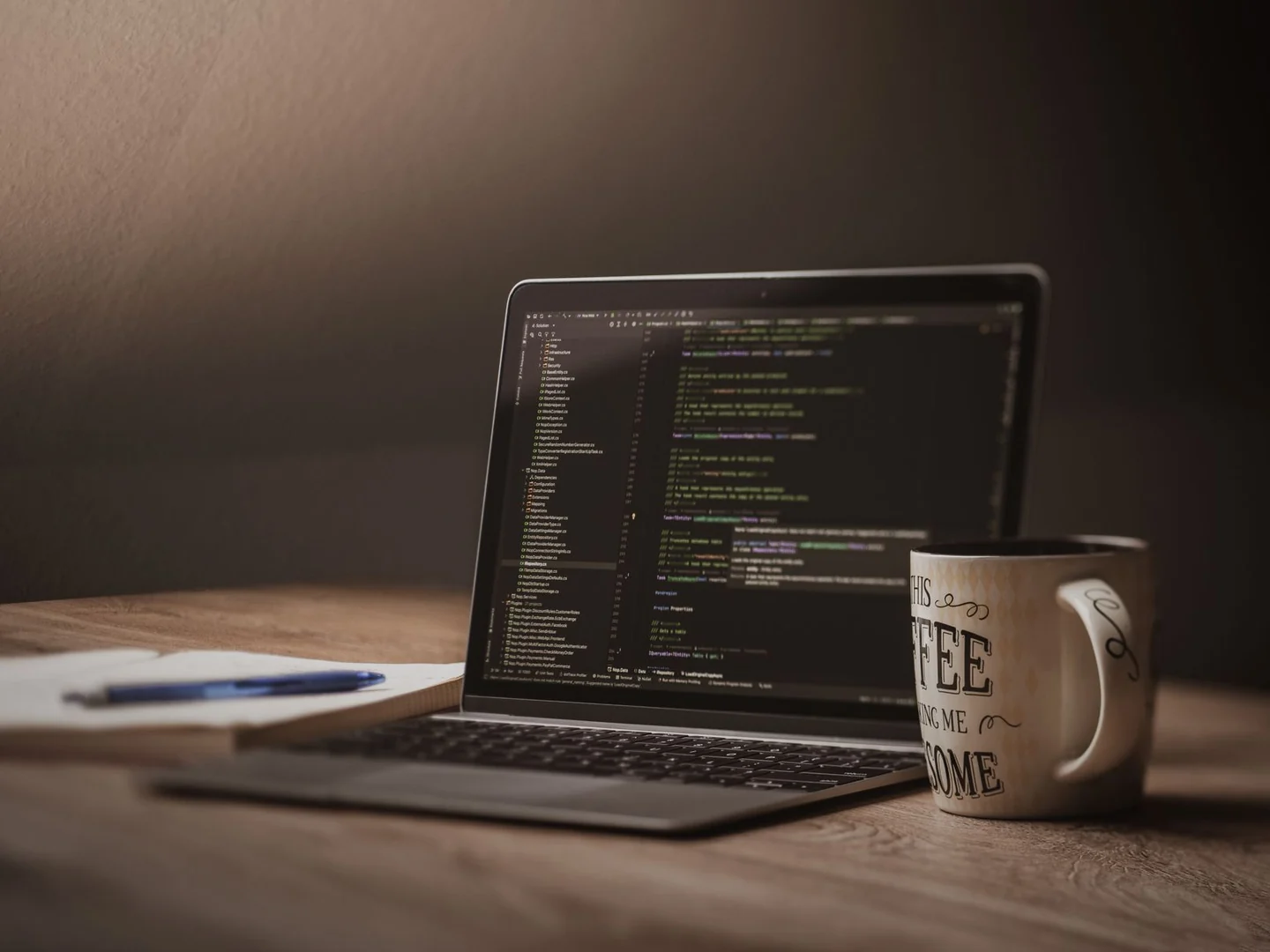 Focused laptop workspace with code, notebook and coffee